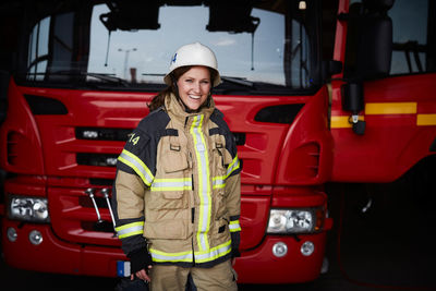 Portrait of smiling female firefighter standing in front of fire engine at fire station