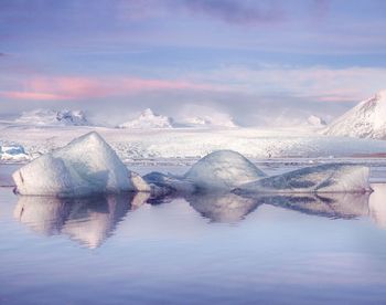 Icebergs in sea against cloudy sky