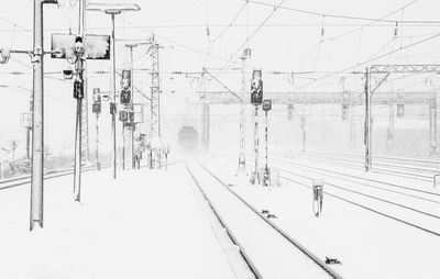 Electricity pylon by snow covered railroad tracks