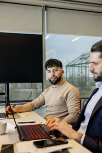 Portrait of young businessman with male colleague at desk in coworking office