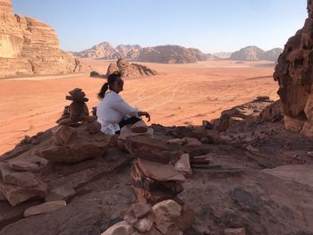 Woman sitting on rock against sky