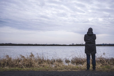 Rear view of man standing on lake against sky