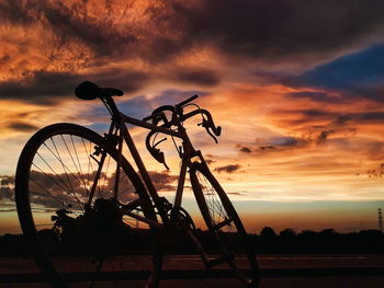 Silhouette bicycle against dramatic sky during sunset