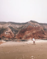 Man walking on a beach against cliffs