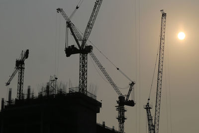 Low angle view of silhouette cranes against sky at sunset