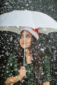 Young woman with umbrella during snowfall against black background