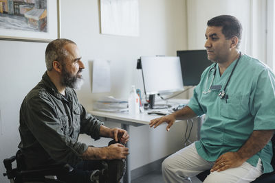 Mature doctor discussing with patient sitting in wheelchair at hospital