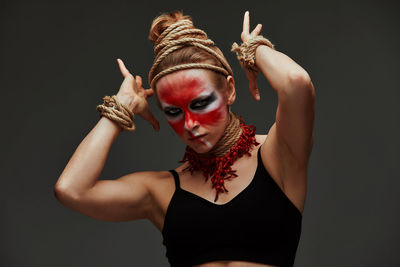 Portrait of young woman with arms raised against black background