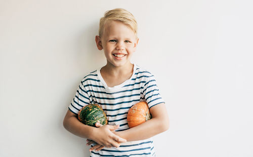 Caucasian blond boy against the background of a white wall holds two pumpkins