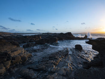 Rocks on beach against sky during sunset