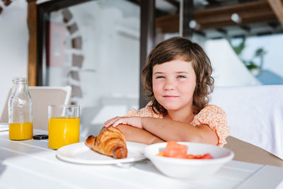 Delightful preschool kid looking at camera while sitting at table with food in cafeteria