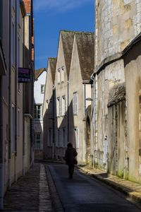 Rear view of man walking on narrow alley amidst buildings