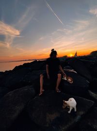 Rear view of people on rock against sky during sunset