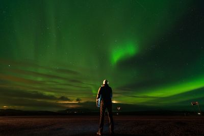 Rear view of man on field against aurora borealis at night