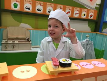 Portrait of cute smiling boy showing peace sign while wearing lab coat