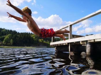 Happy shirtless boy jumping in lake against sky