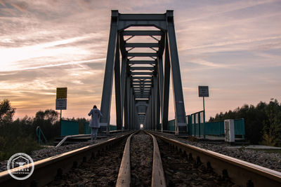 Rear view of man on railroad tracks against sky during sunset