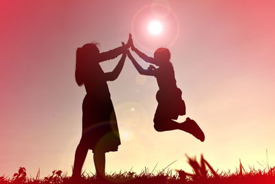 Silhouette mother with daughter on field against sky