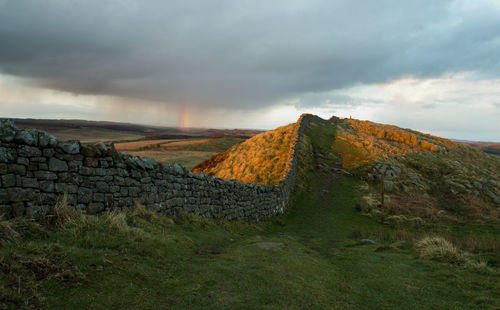 Hadrians wall on field against cloudy sky during sunset