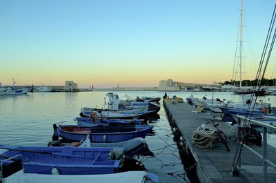 Boats moored in harbor at sunset