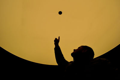 Silhouette man playing with ball against sky during sunset