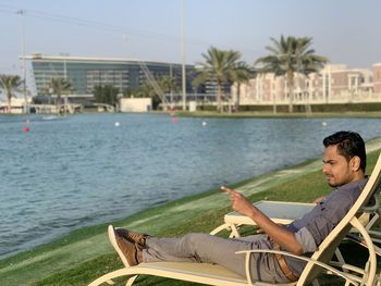 Side view of young man sitting on lounge chair at lakeside