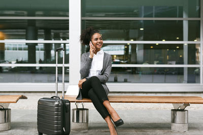 Woman talking on mobile phone while sitting on bench at airport