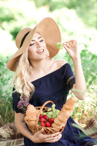 Smiling woman wearing hat holding basket of fruits looking away