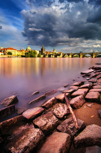 Scenic view of lake by buildings against sky during sunset