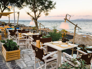 Chairs and tables at restaurant by sea against sky