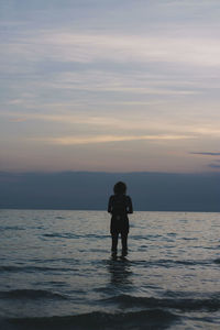 Silhouette man standing in sea against sky during sunset