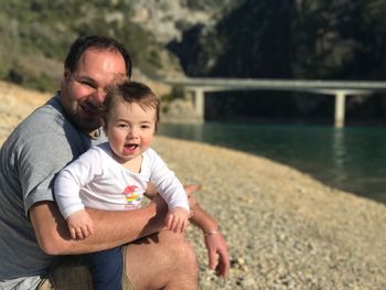 Portrait of happy father holding son while sitting by lake of sainte-croix