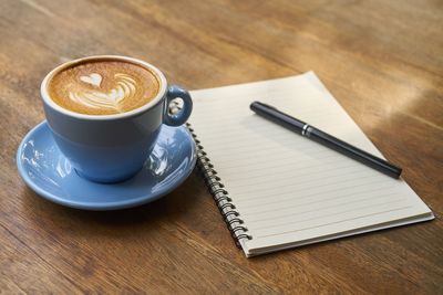 High angle view of coffee cup with diary and pen on table