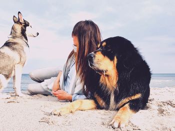 Woman with dog relaxing at beach against sky