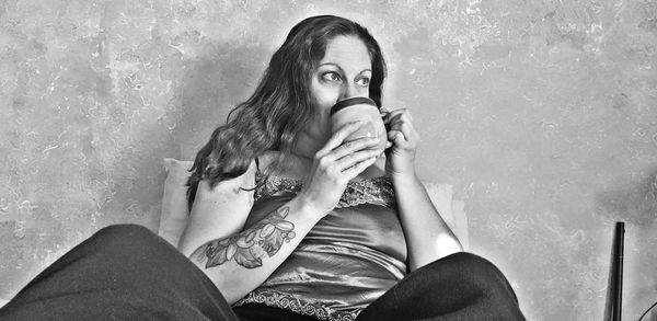 Low angle view of woman drinking coffee while sitting against wall