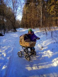 Woman with baby stroller on snow covered field against trees