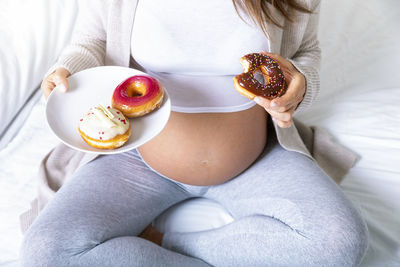 Midsection of pregnant woman having donut at home