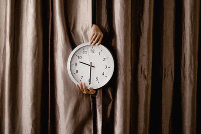 Close-up of hands holding clock by curtain