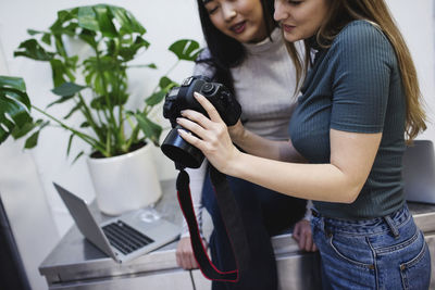 Female bloggers watching photographs on digital camera in creative office