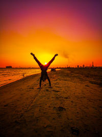 Silhouette person with arms raised on beach against sky during sunset