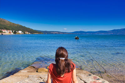 Girl with a red shirt staring at the sea and a little boat