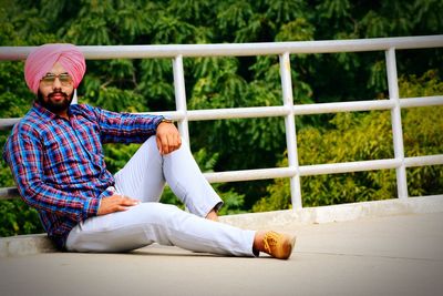 Portrait of confident young man wearing turban sitting on footbridge