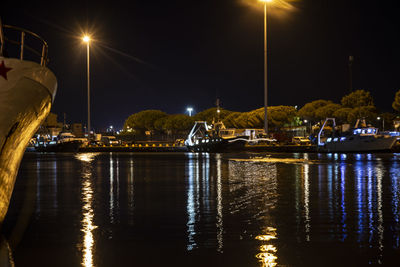 Illuminated city by river against sky at night