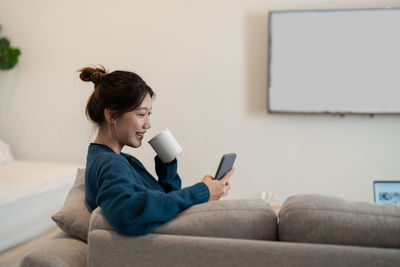 Young woman using mobile phone while sitting on sofa at home