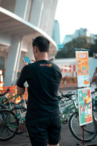 Rear view of man standing on bicycle in city