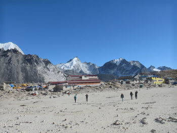 People on beach by mountains against clear blue sky