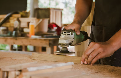 Asian carpenter is sanding wood using an electric wood sander to smooth the wood surface 