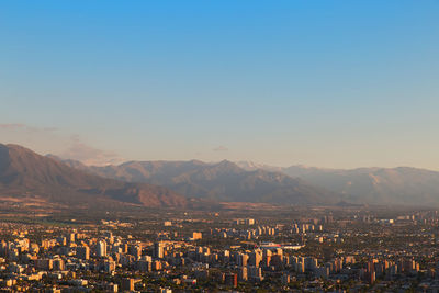 Aerial view of city by mountains against clear sky