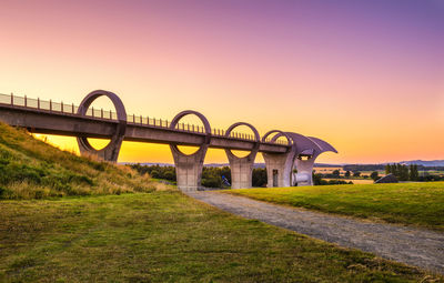 Arch bridge on field against sky during sunset