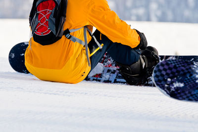 Low section of person with snowboard sitting on snow